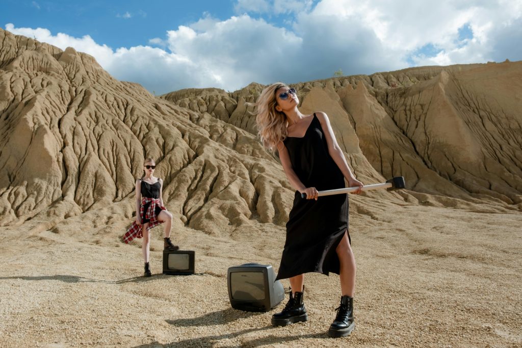 Two women in the desert ready to smash small TVs with sledgehammers