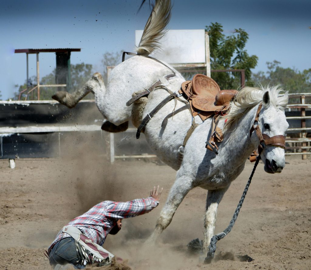 Man who has been thrown by a kicking horse, surrounded by dust from its hooves