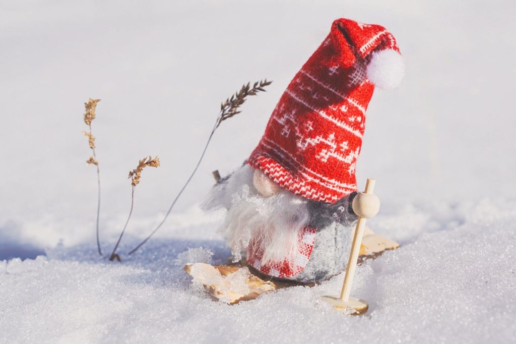 Tiny fabric gnome figurine with a red knitted hat in the snow, skiing. Image by Susanne Jutzeler.